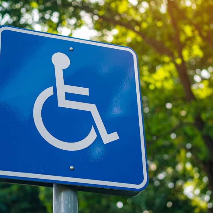Blue disabled access road sign set against lush green trees, accessibility symbol, public infrastructure, inclusive urban environment. Close-up.